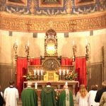 Photo of priests facing altar vested in green, with congregation and servers.